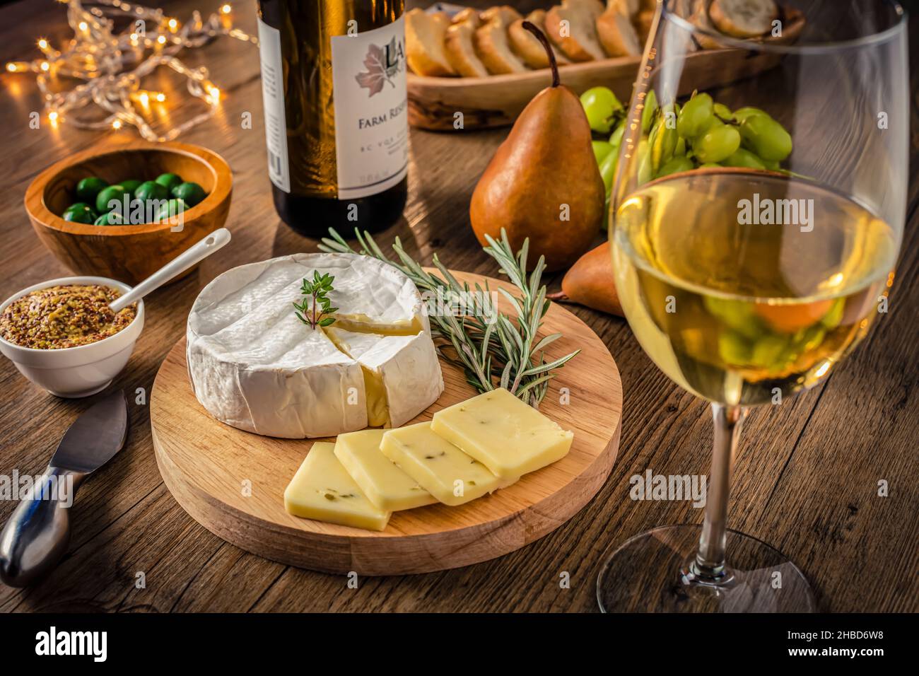 Vin et fromage de fête avec fromage et verre de vin blanc, poires, raisins et olives, lumières scintillantes sur fond de bois. Banque D'Images