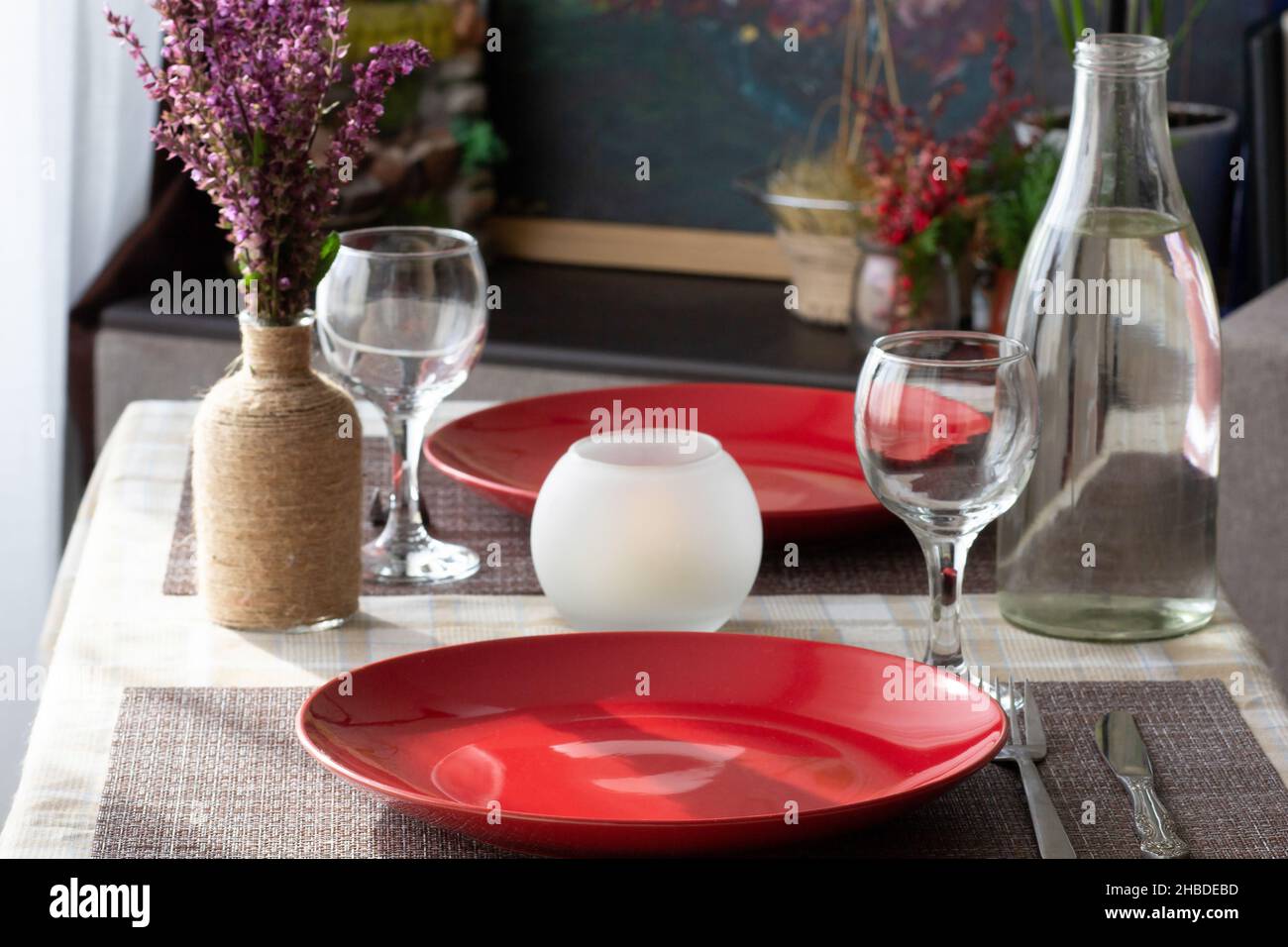 Table avec vaisselle: Vide sans repas assiettes rouges, verres à vin, bouteille d'eau et couteau et fourchette pour dîner romantique pour deux personnes à la maison Banque D'Images