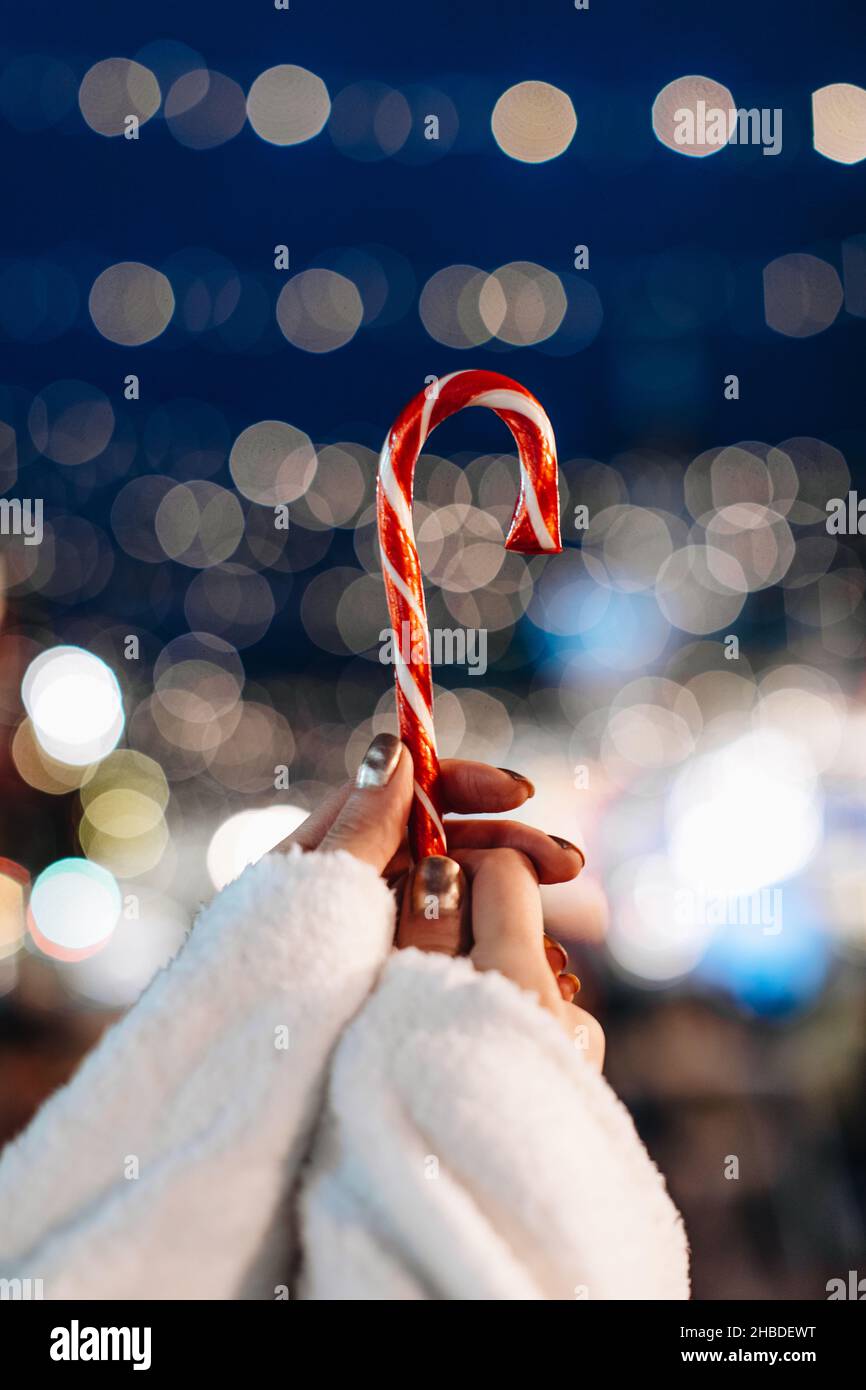 Mains de femmes tenant rouge blanc canne douce lollipop sur le fond de bleu argent fée lumières.Détails magiques de Noël Banque D'Images