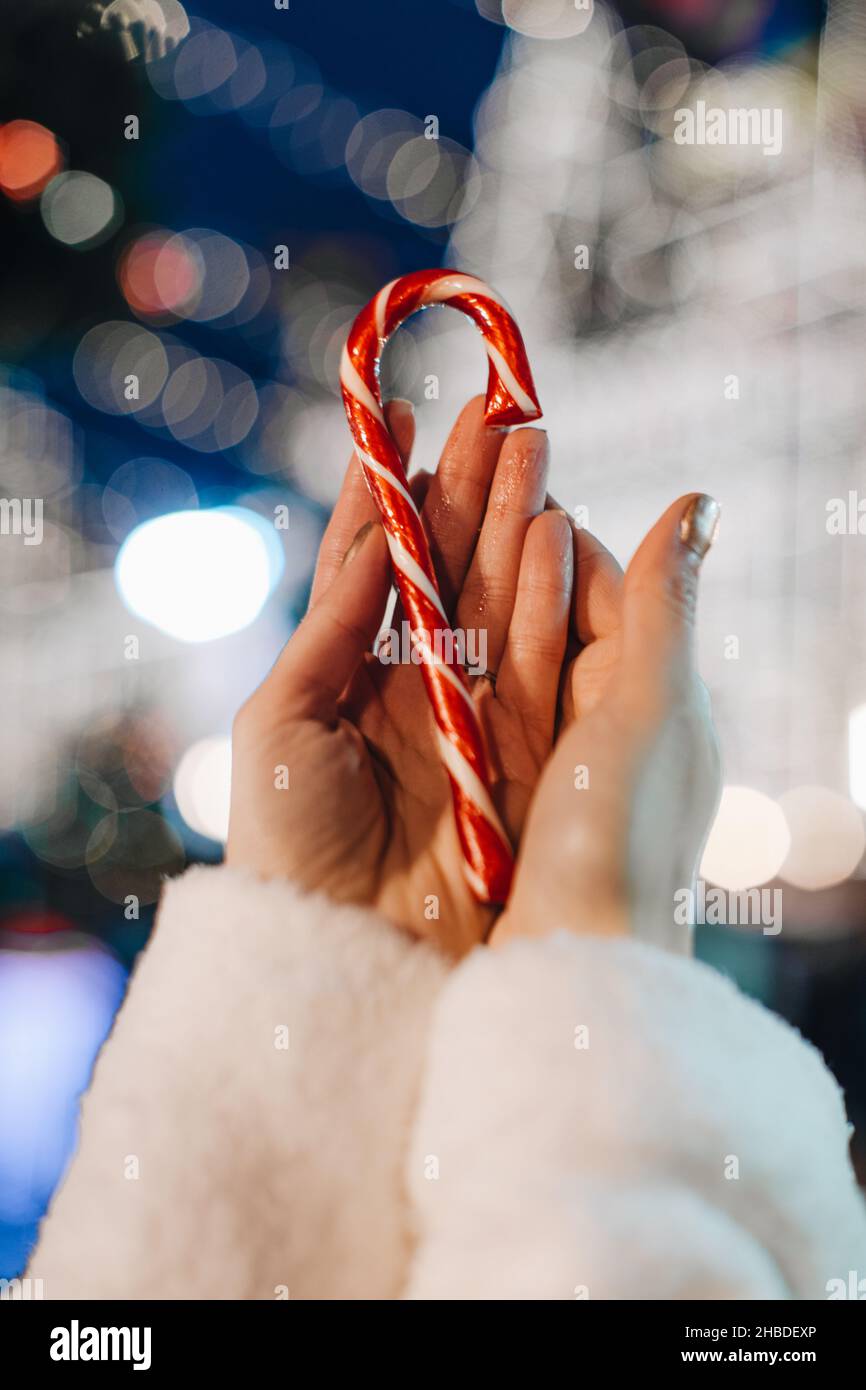 Mains de femmes tenant rouge blanc canne douce lollipop sur le fond de bleu argent fée magie lumières.Détails des vacances de Noël Banque D'Images