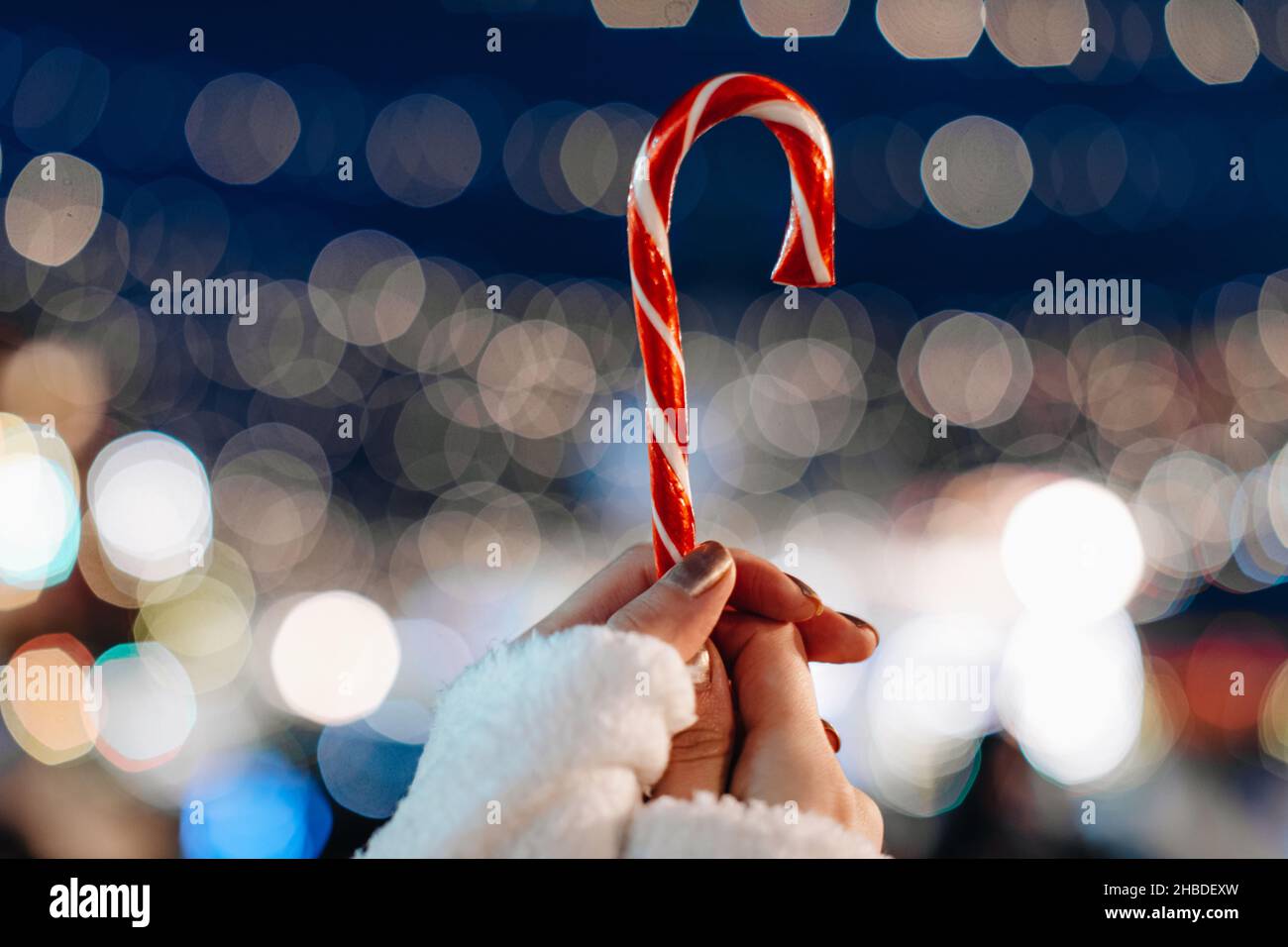 Mains de femmes tenant rouge blanc canne douce lollipop sur le fond de bleu argent fée lumières.Détails magiques de Noël Banque D'Images