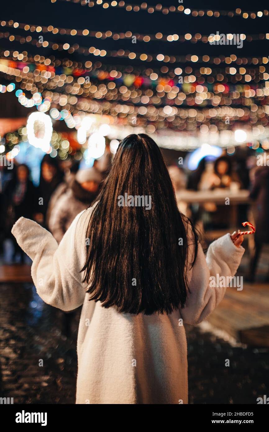 Jeune femme brune en blanc long manteau de fourrure d'hiver au marché de Noël avec des lumières magiques dorées Banque D'Images