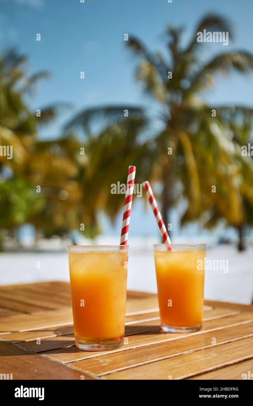 Deux boissons fraîches rafraîchissantes sur la plage de sable blanc.Verres de cocktails avec pailles à boire en papier sur une table en bois contre des palmiers. Banque D'Images