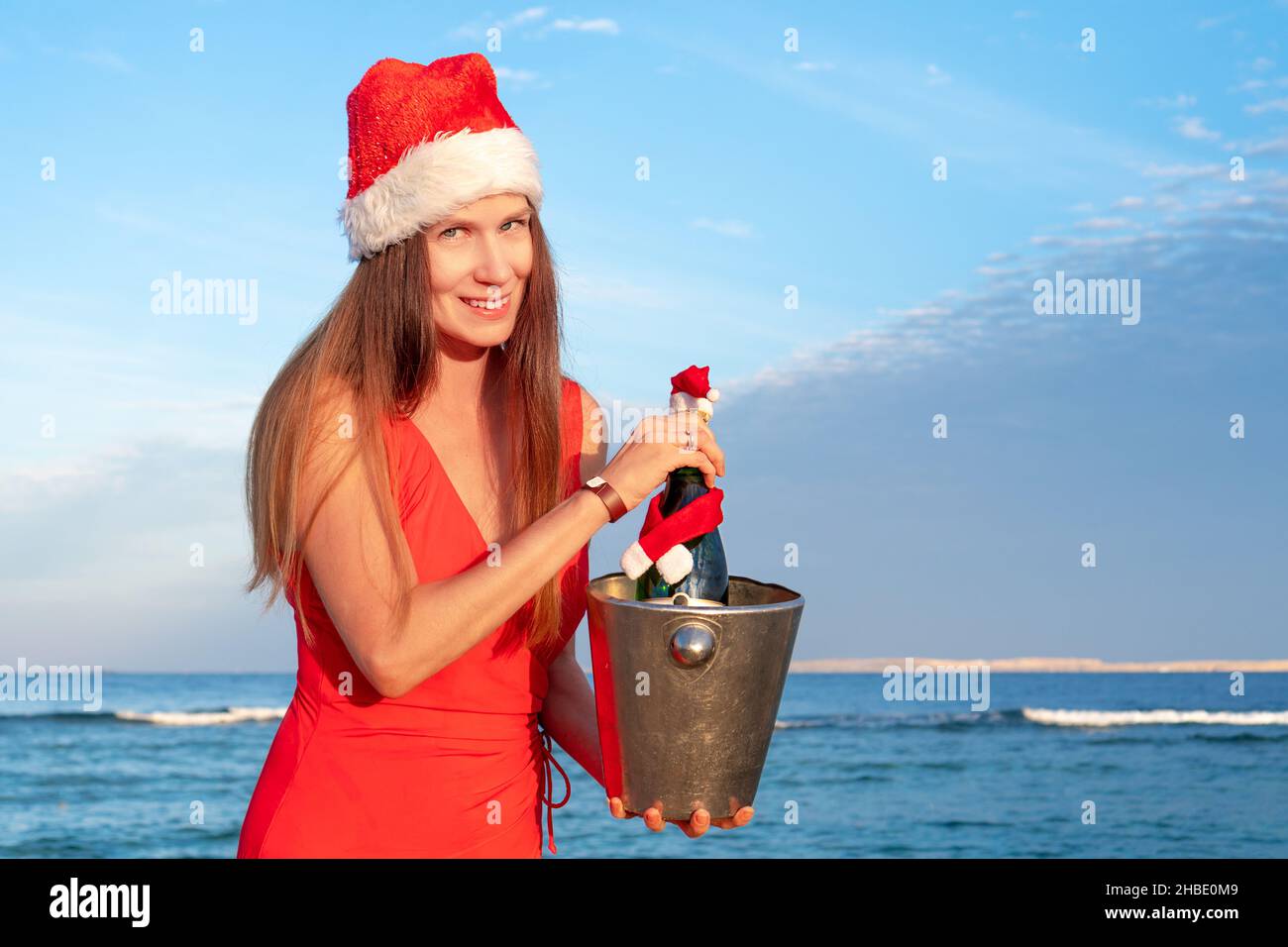 Une belle jeune fille dans un chapeau de Père Noël tient une bouteille de  champagne dans un seau à glace contre la mer bleue.Concept de Noël Photo  Stock - Alamy