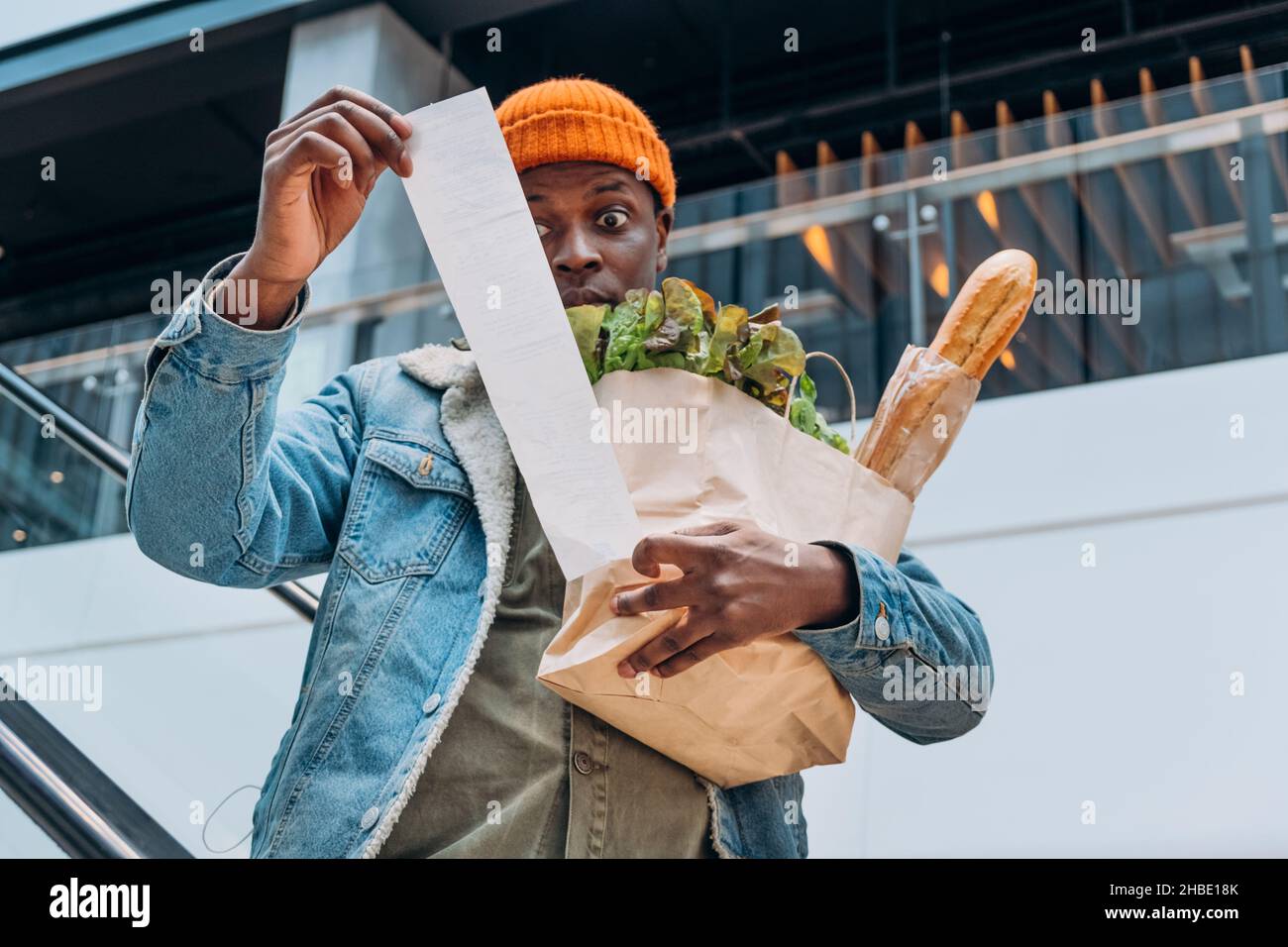 Doutant de la personne afro-américaine dans une veste en denim, regarde le lot de conservation total des reçus de papier de vente avec les produits alimentaires sur l'escalier roulant Banque D'Images