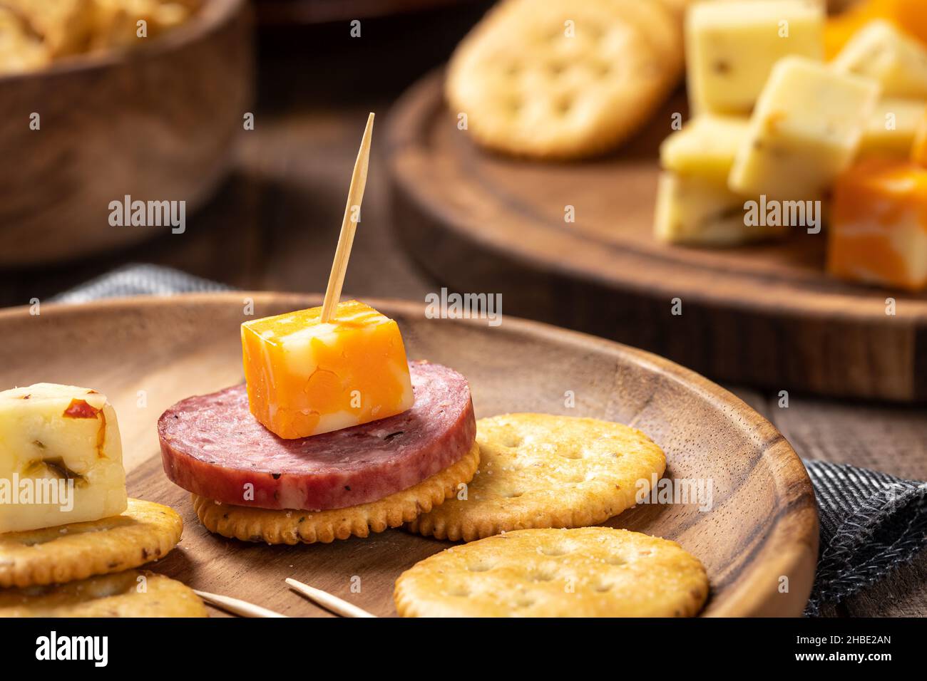 Gros plan de salami en tranches, de cubes de fromage et de craquelins sur une assiette en bois Banque D'Images