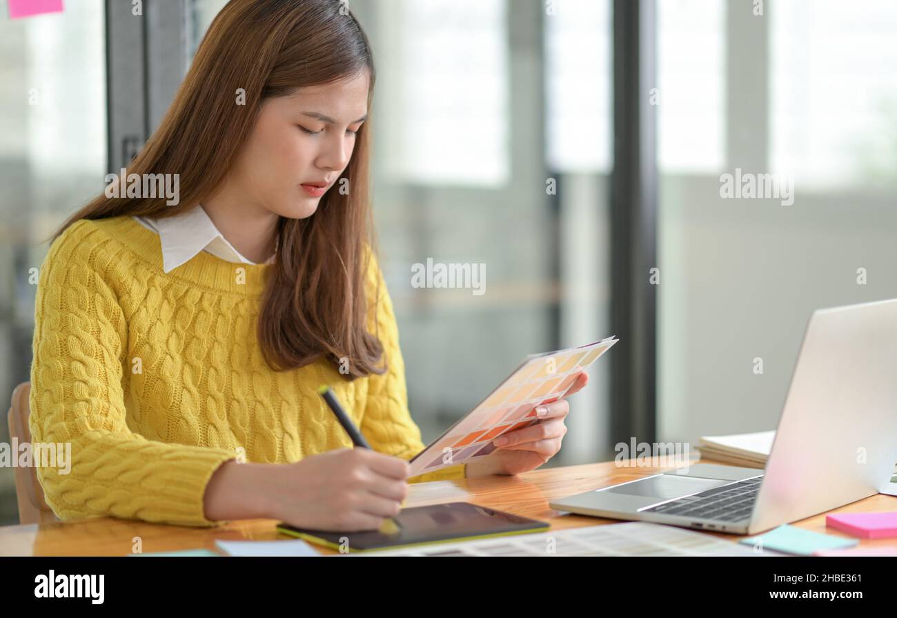 Un concepteur indépendant tient un chargeur de couleurs à portée de main, en esquissant sur une tablette numérique. Banque D'Images