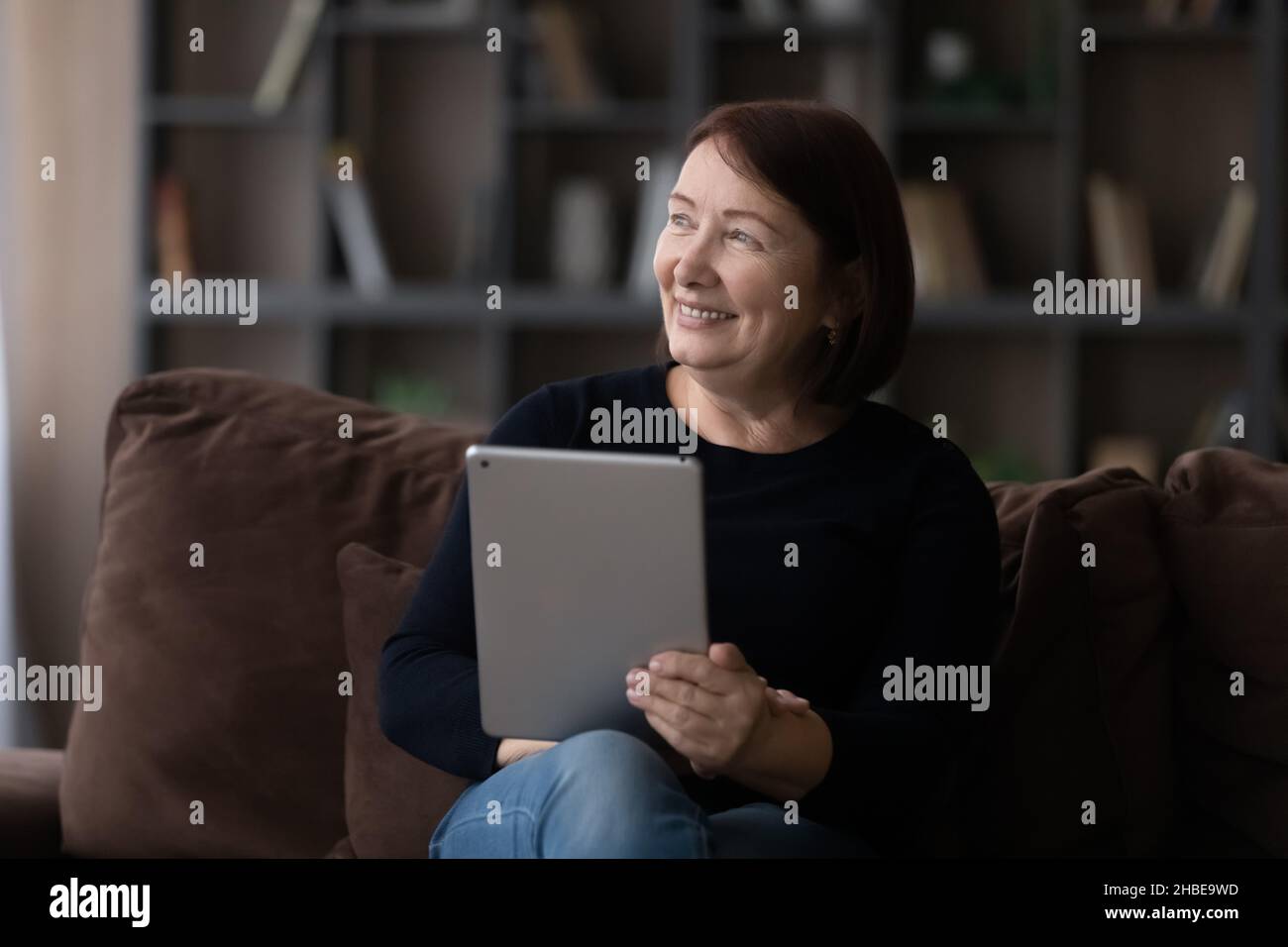 Une femme âgée se détende sur un canapé avec une tablette électronique regarder de côté Banque D'Images