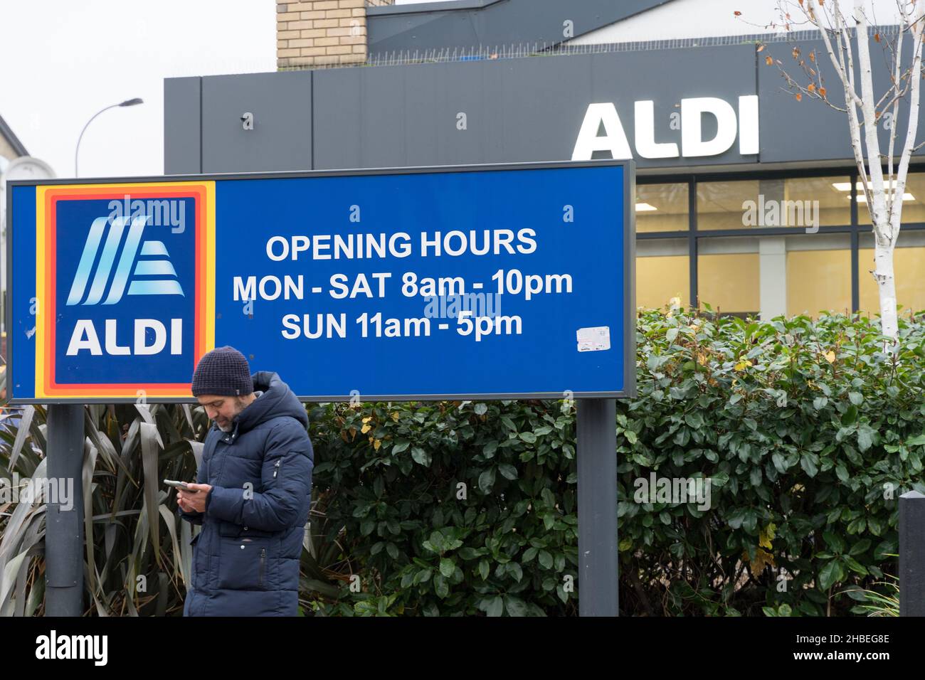 Un client qui fait la réservation d'un taxi à côté des horaires d'ouverture du magasin et du logo devant le supermarché ALDI de Londres Banque D'Images