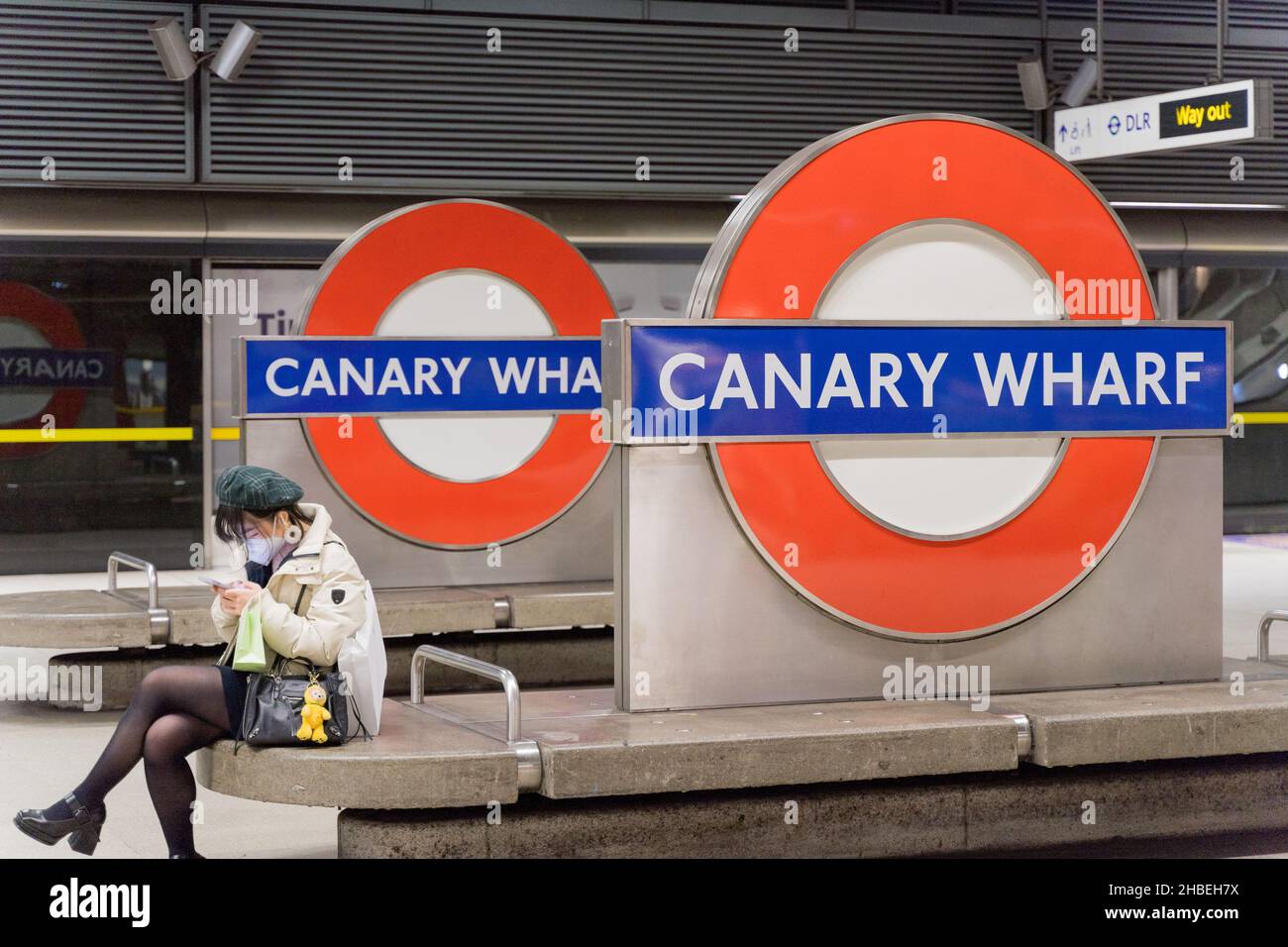 Une femme passager en tube masque portant un chapeau est assise sur le banc de la station en attendant son train à la station de métro Canary Wharf London Angleterre Royaume-Uni Banque D'Images