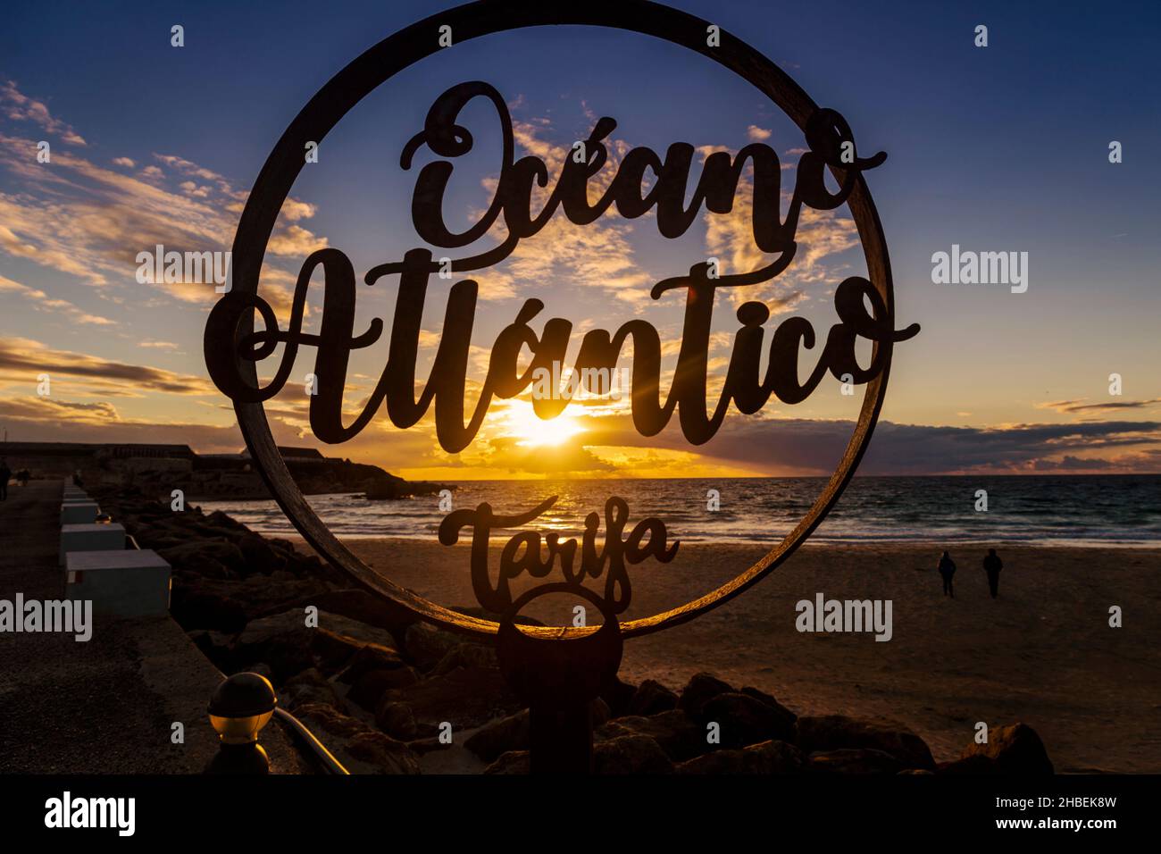 Silhouette d'Oceano Atlantico Tarifa signe et deux personnes marchant sur la plage au coucher du soleil, Tarifa, Cadix, Andalousie, Espagne Banque D'Images