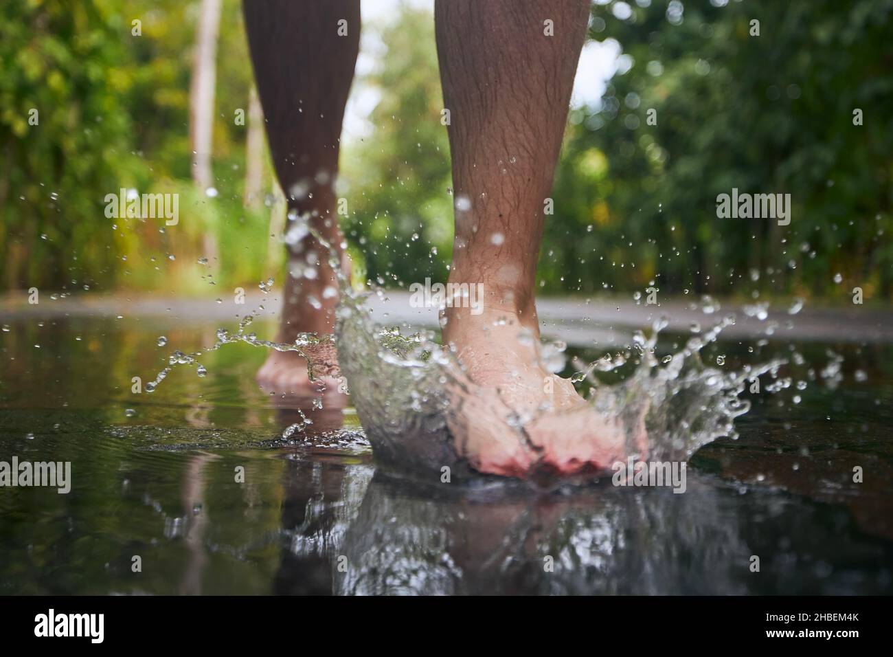 Pied pieds nus d'un jeune homme qui marche jusqu'à la flaque et qui éclabousse de l'eau pendant les jours de pluie. Banque D'Images