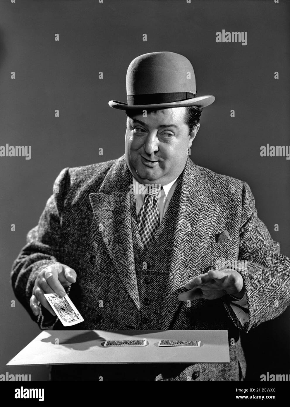 Homme bien habillé en costume 3 pièces et chapeau de bowling faisant un tour de carte.Vers 1940 Banque D'Images
