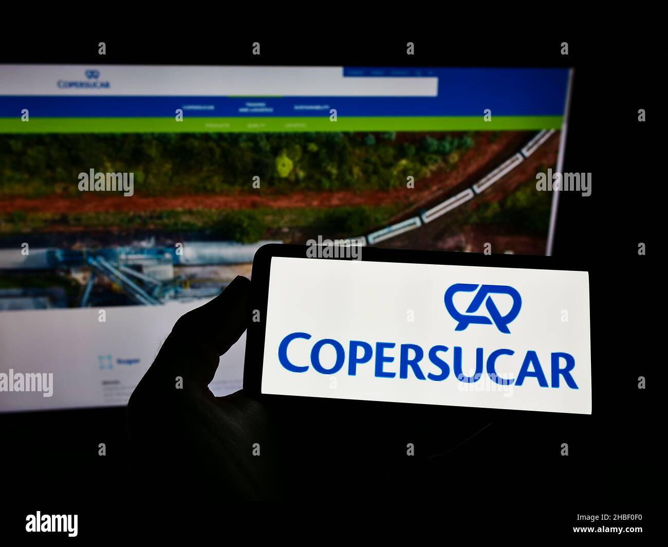 Personne tenant smartphone avec logo de la société brésilienne de sucre et d'éthanol Copersucar S.A. sur écran devant le site.Mise au point sur l'affichage du téléphone. Banque D'Images