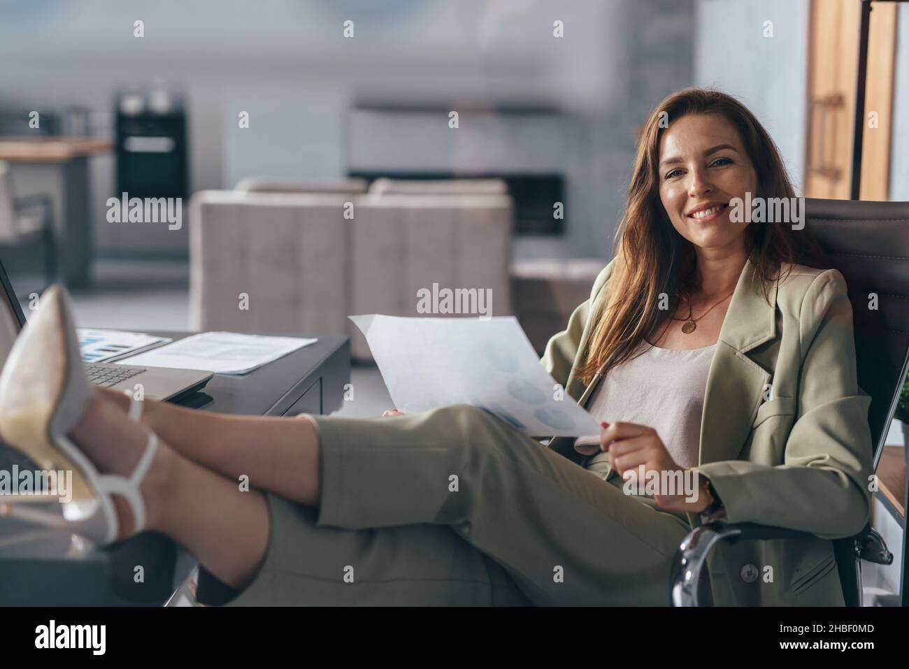 Femme tenant une feuille de papier, travaillant à la maison avec ses pieds sur son bureau. Banque D'Images