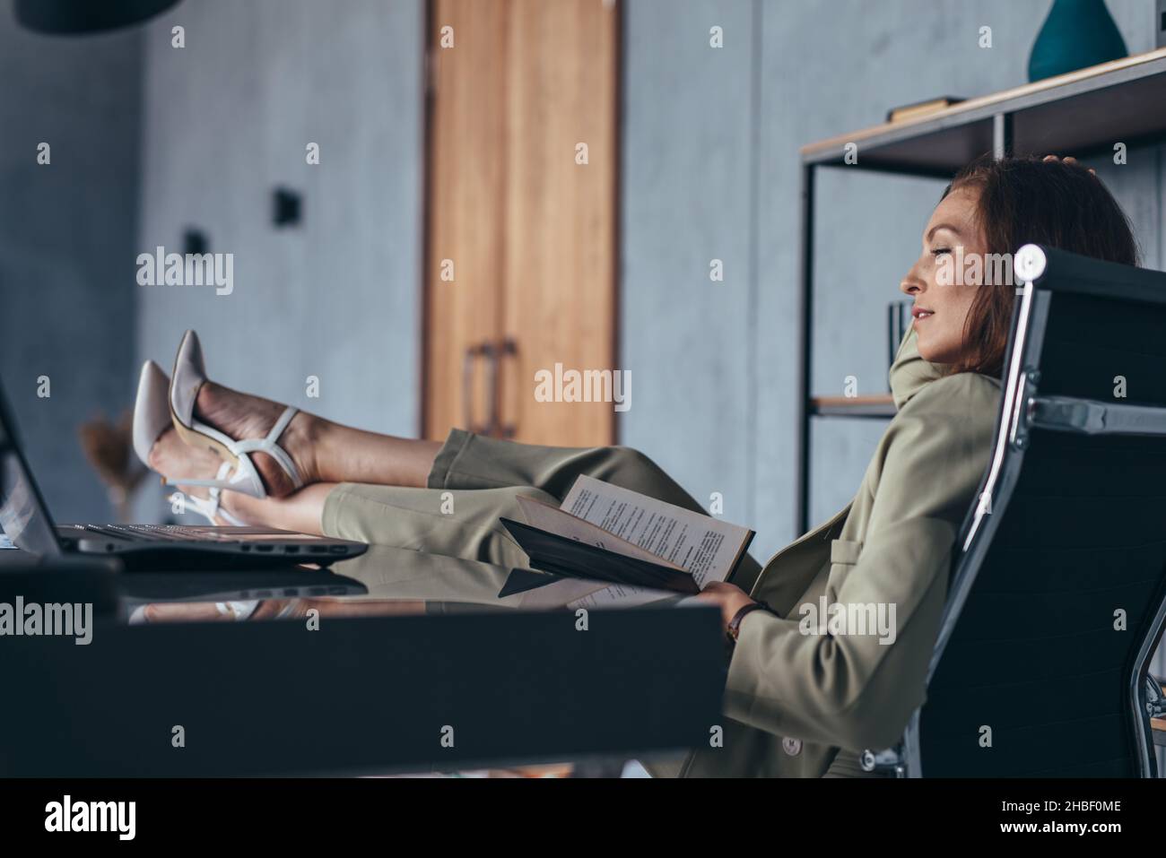 Elle s'assoit avec ses pieds sur son bureau. Banque D'Images