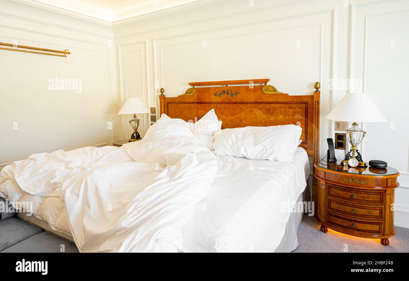 Lit non fait avec literie, draps et draps froissés dans une chambre d'hôtel vide et luxueuse Banque D'Images