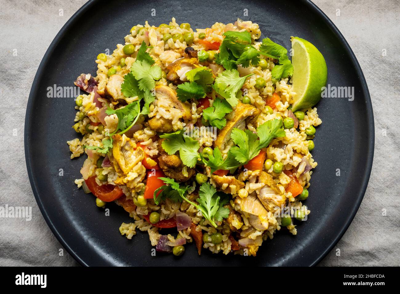 Curry de poulet aux pois verts, poivron rouge, coriandre, citron vert et riz basmati, servi dans un plat sombre. Banque D'Images