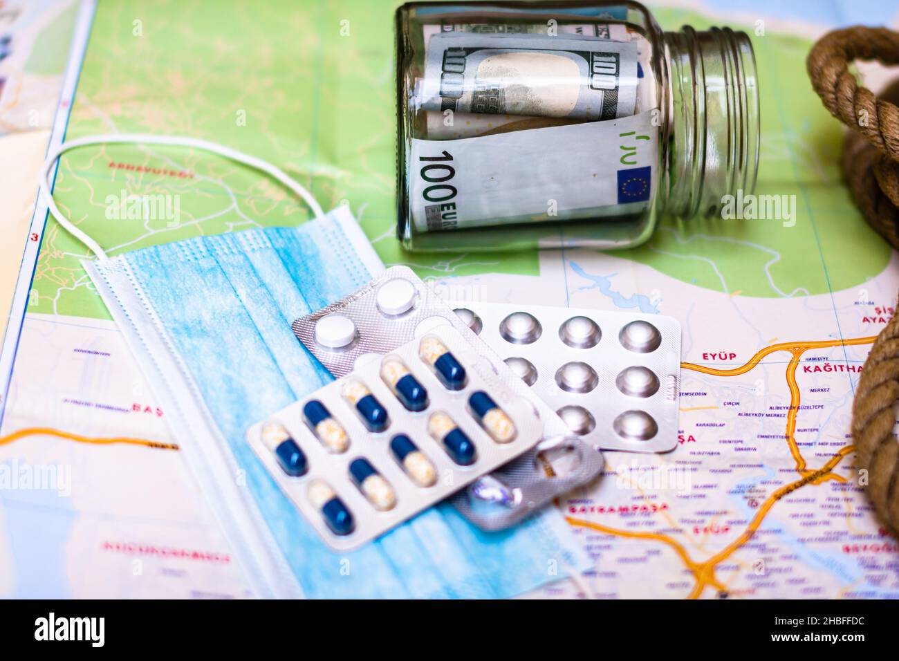 Un pot en verre avec des billets de banque, des pilules et un masque chirurgical sur la carte Banque D'Images