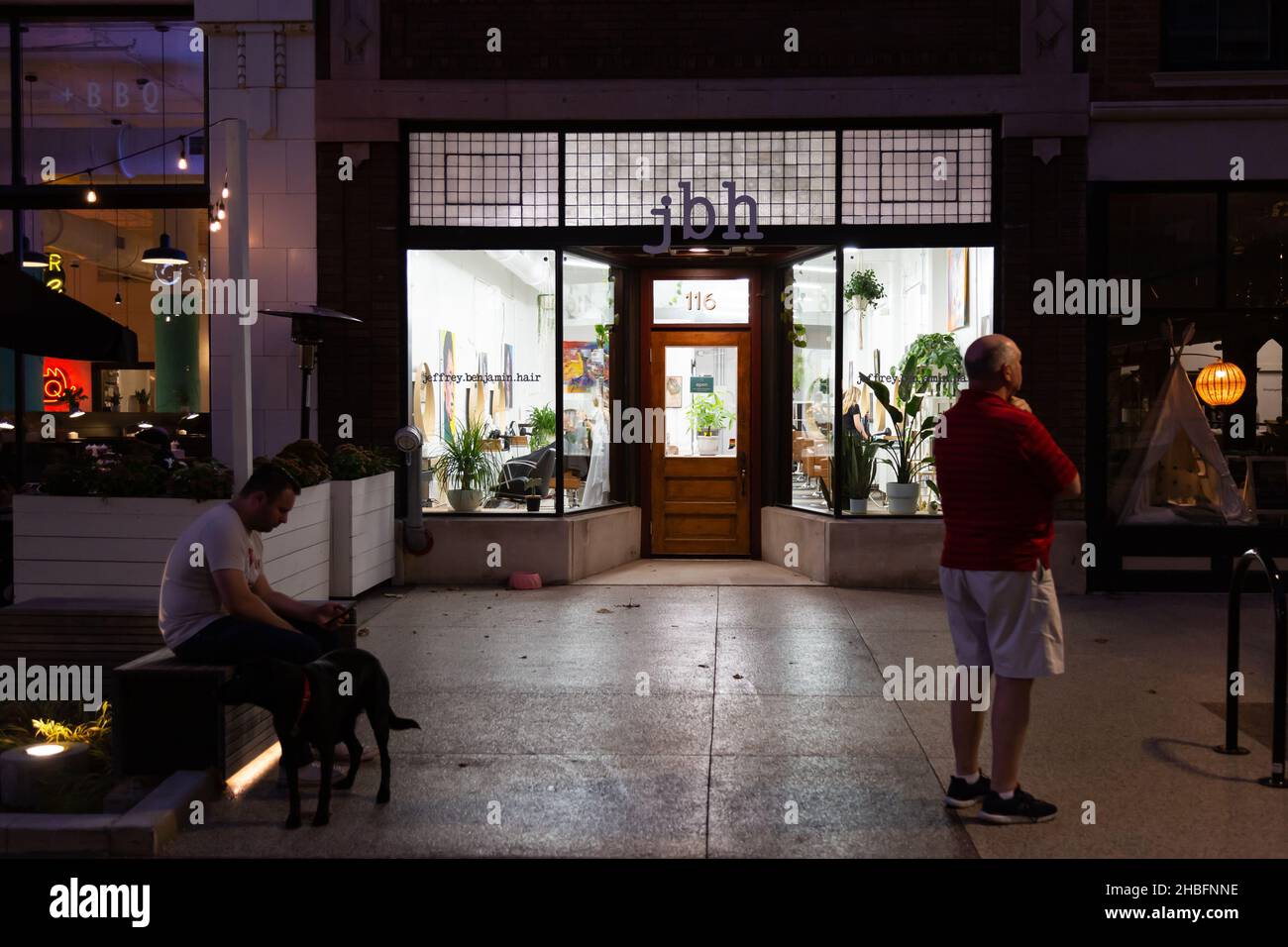 Deux hommes et un chien à l'extérieur branché Jeffrey Benjamin cheveux la nuit sur le Landing dans le centre-ville de fort Wayne, Indiana, États-Unis. Banque D'Images