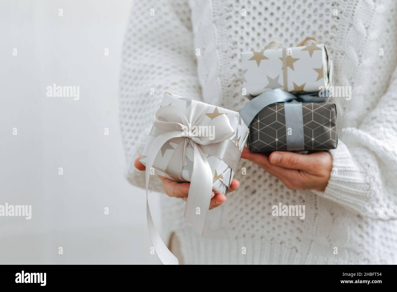 Une fille en chandail blanc tient des cadeaux de vacances.Les mains des femmes tiennent des boîtes de vacances.Le concept de la préparation des vacances Banque D'Images