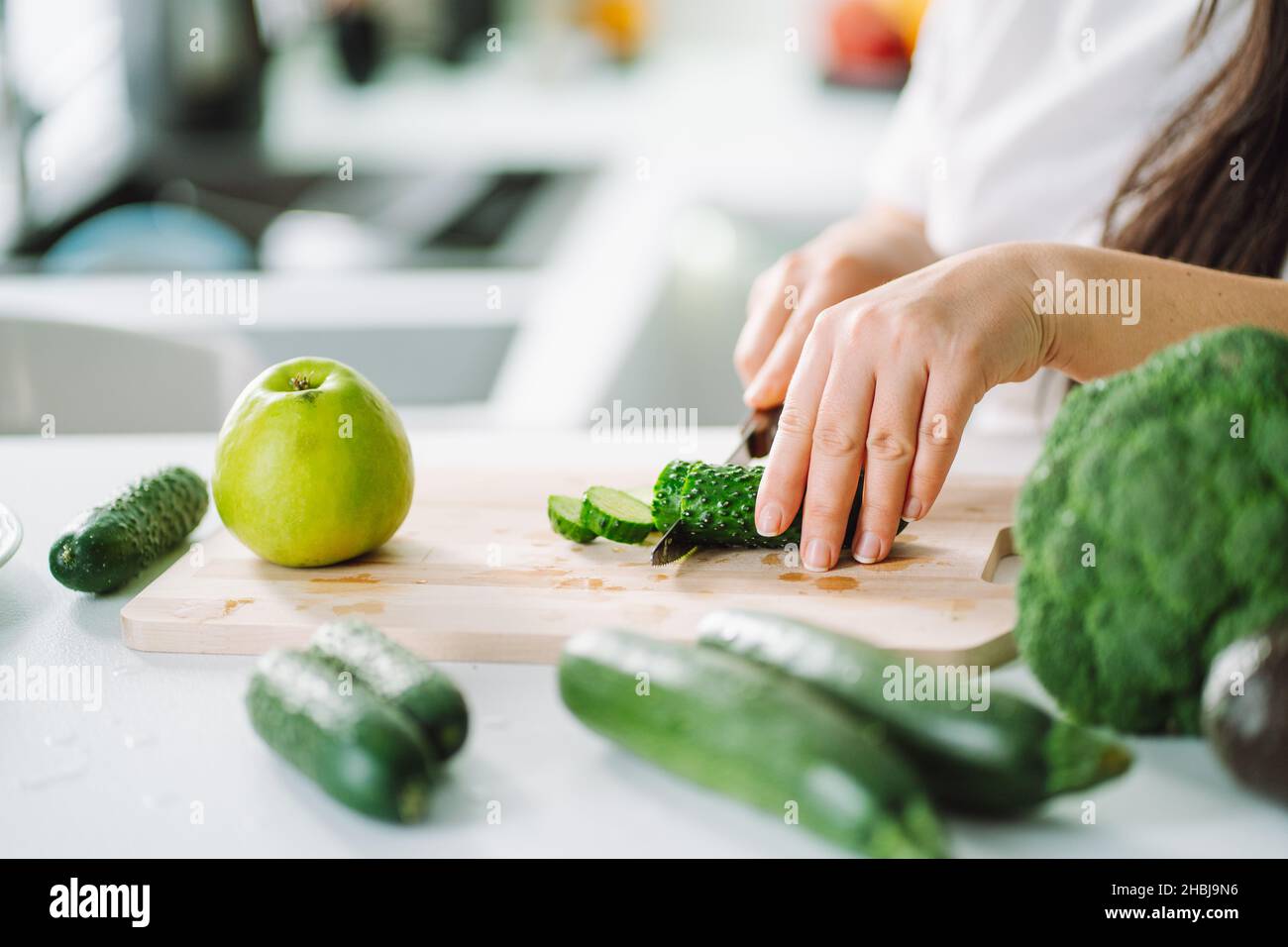 Femme préparant de la nourriture dans sa cuisine.Une femme hache des légumes verts frais sur une planche à découper dans une cuisine légère.Alimentation saine, désintoxication, alimentation Banque D'Images