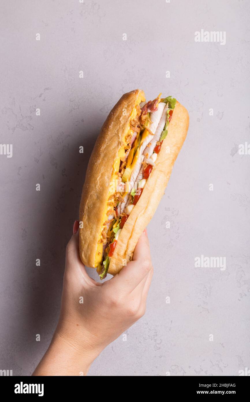 la main de femme tient le sandwich sur le mur gris ombres dures. Concept de promotion des sandwichs Banque D'Images