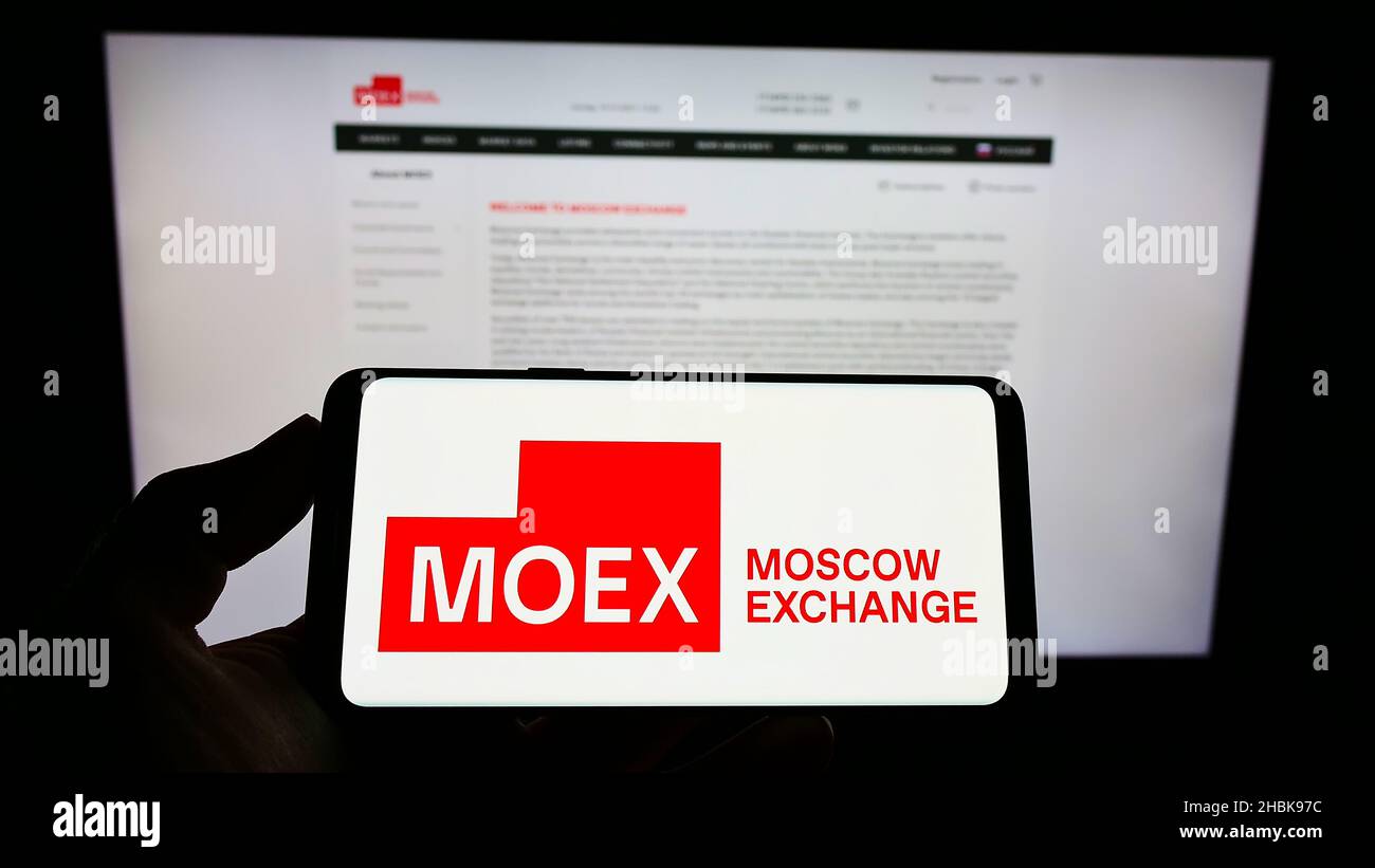 Personne tenant un smartphone avec le logo de la bourse russe Moscow Exchange (MOEX) à l'écran devant le site.Mise au point sur l'affichage du téléphone. Banque D'Images