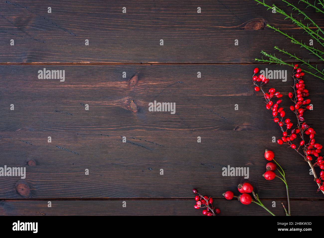 Hiver et arrière-plan de Noël.Branches de chien rose avec hanche rose, barberry rouge sur table rustique en bois brun foncé.Modèle de conception Flat Lay. Banque D'Images