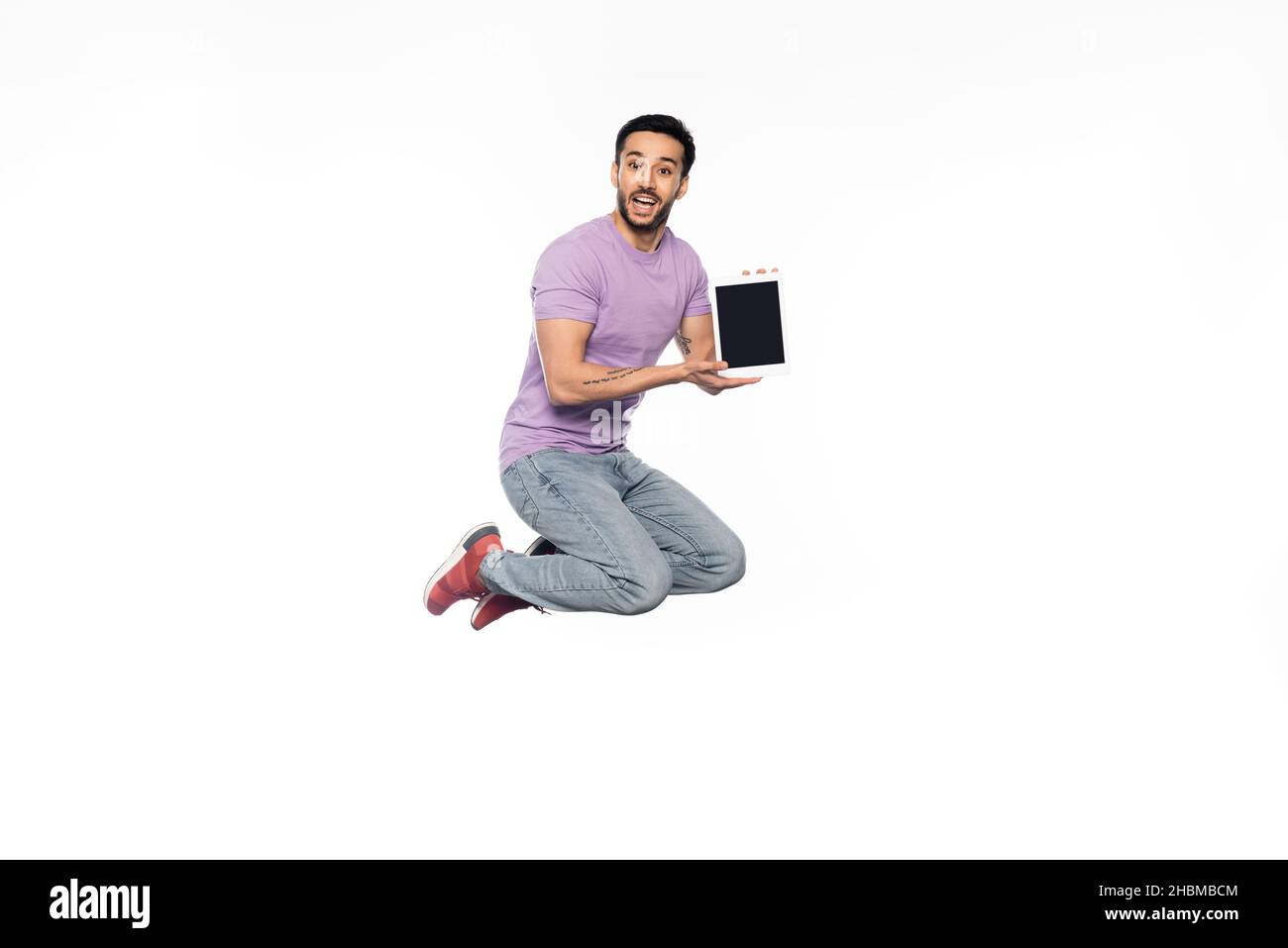 un homme émerveillé avec un jean et un t-shirt violet qui se levent tout en tenant la tablette numérique sur le blanc Banque D'Images