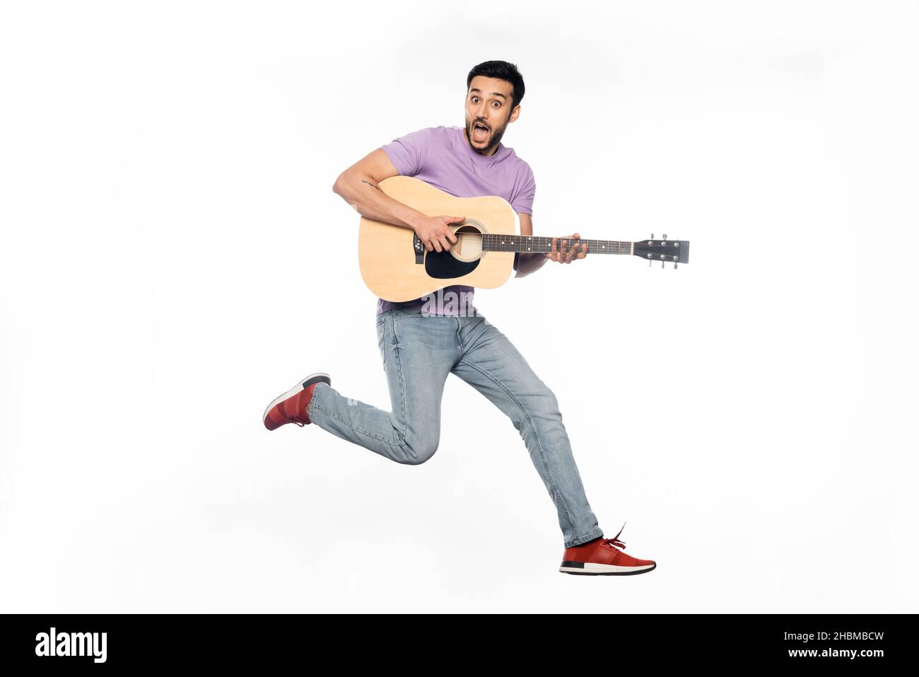 un homme émerveillé dans un jean et un t-shirt violet en jouant de la guitare acoustique sur le blanc Banque D'Images