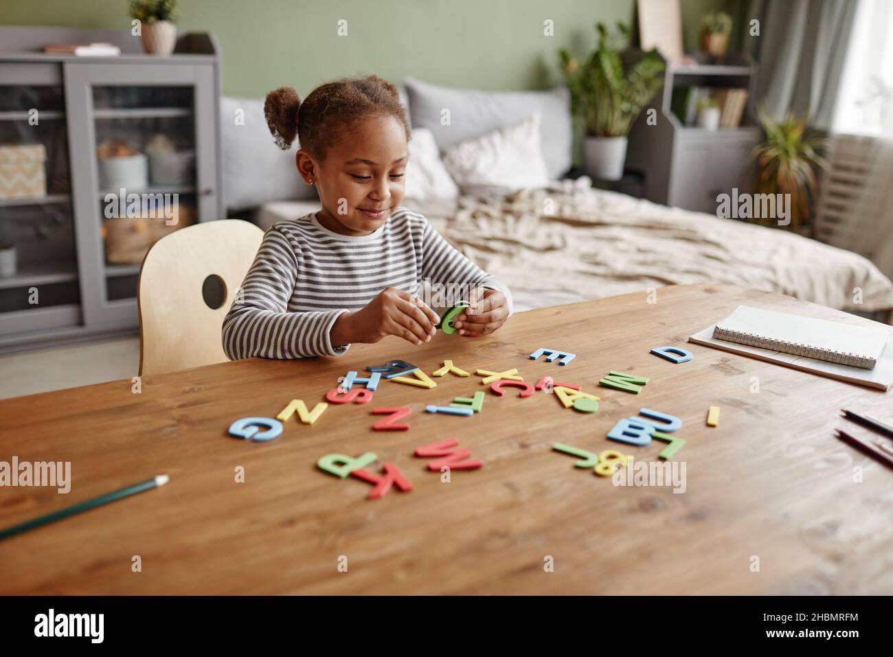 Portrait d'une adorable fille afro-américaine jouant avec des lettres tout en étudiant à la maison, espace de copie Banque D'Images