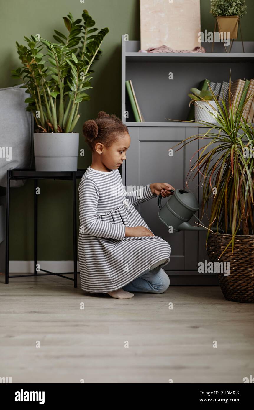 Portrait de la vue latérale pleine de mignons fille afro-américaine arrosoir des plantes à la maison Banque D'Images