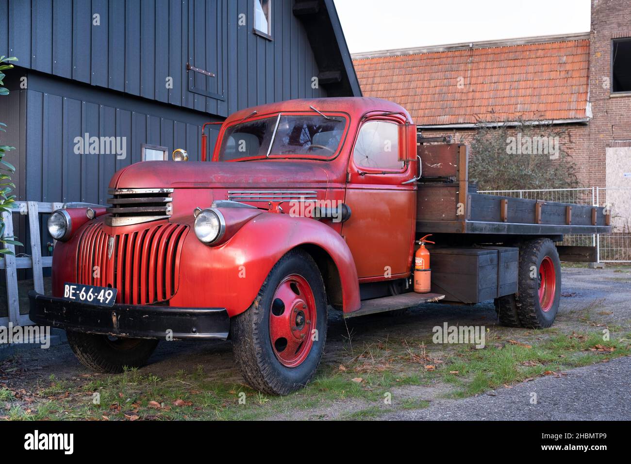 Vieux pick-up Chevrolet rouge de 1942 avec plate-forme de chargement en bois et enregistrement néerlandais, debout devant un hangar Banque D'Images