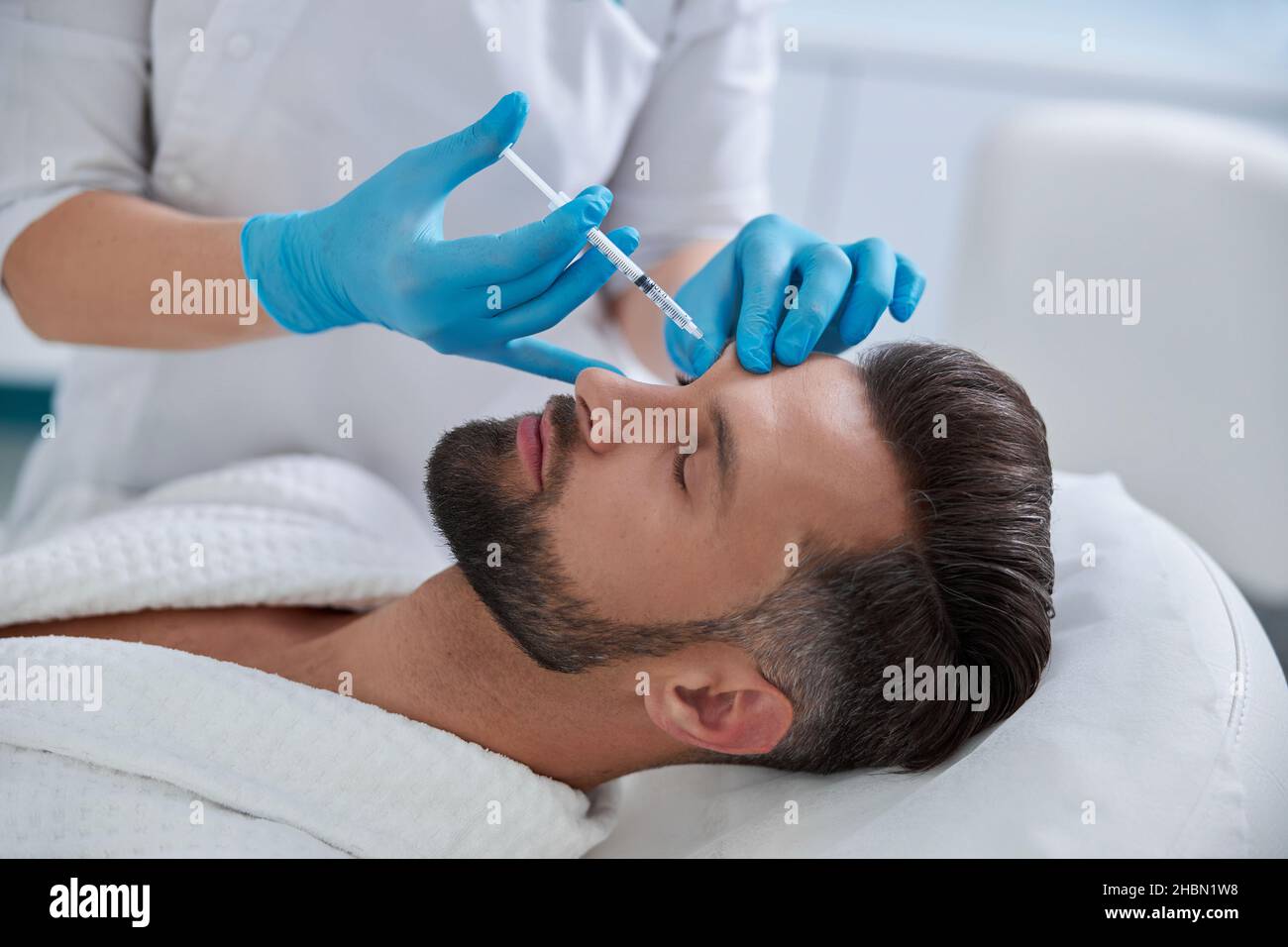 Esthéticienne en gants bleus fait l'injection à la procédure de levage des sourcils au patient mature dans la clinique Banque D'Images