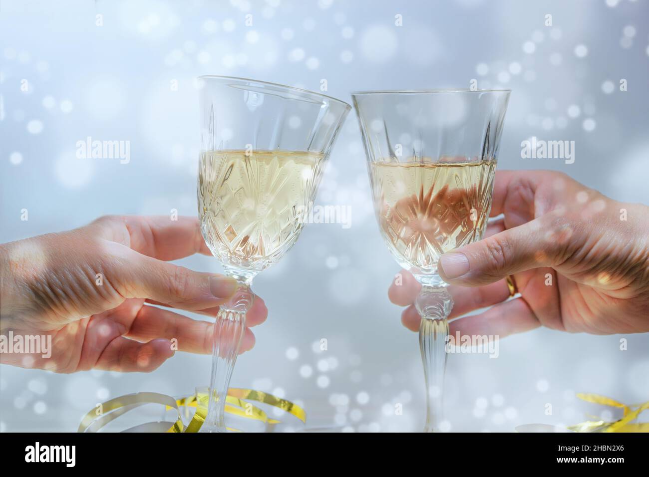 Toast à deux mains avec des verres à champagne lors d'une fête du nouvel an ou de Noël, fond clair et enneigé, mise au point sélectionnée, profondeur de champ étroite Banque D'Images