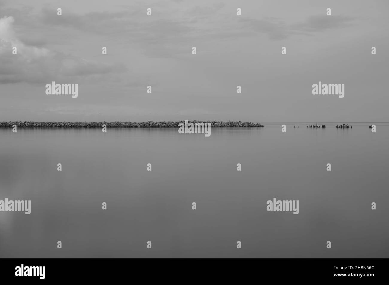 un vieux quai en pierre avec une rive et des nuages dans le ciel et un reflet dans l'étendue calme de l'eau Banque D'Images