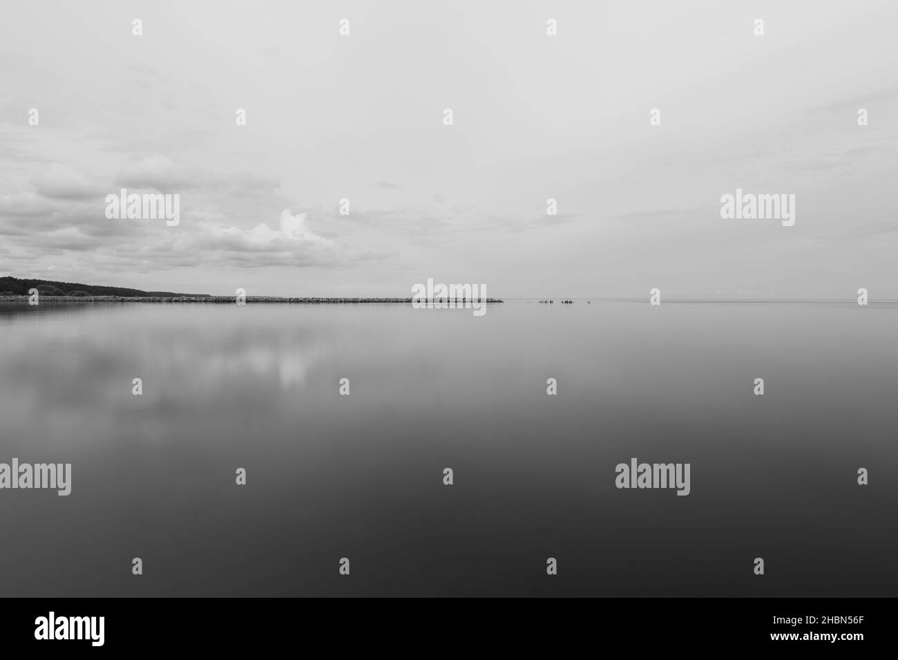 un vieux quai en pierre avec une rive et des nuages dans le ciel et un reflet dans l'étendue calme de l'eau Banque D'Images