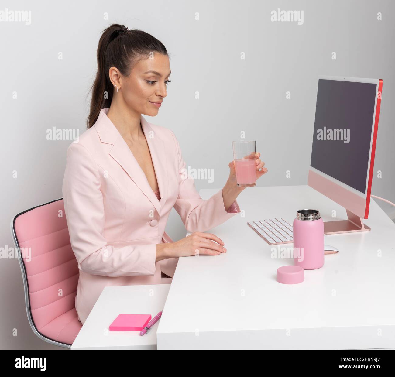 Salisbury, Royaume-Uni.2021. Une employée de bureau boit à partir d'un verre avec une fiole rose sur le bureau. Banque D'Images