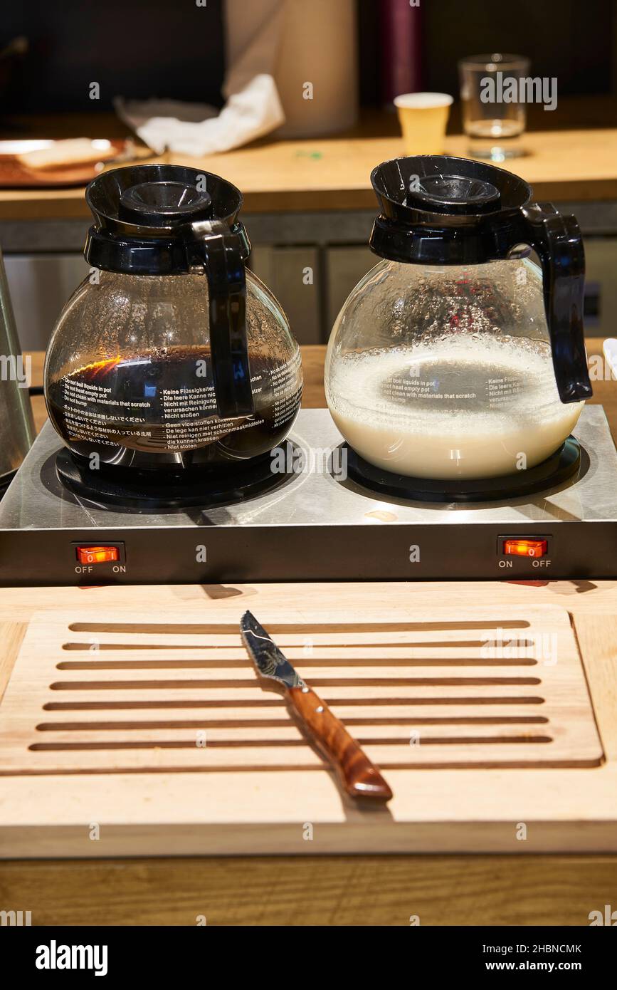 Des cruches de café et de lait sur la base chauffante et un couteau à pain sur une planche à bois dans la salle de petit-déjeuner de l'hôtel Banque D'Images