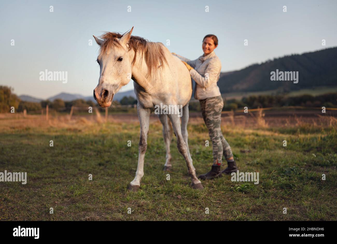 Blanc Arabian Horse, automne après-midi, détail sur la tête, flou souriant jeune femme dans la veste chaude tenant son dos Banque D'Images