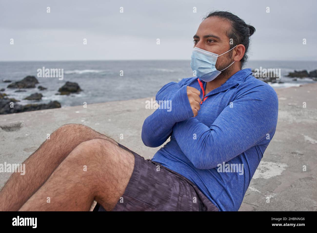 L'homme masqué effectue des sit-ups devant la mer. Nouvelle normalité. Sports Banque D'Images