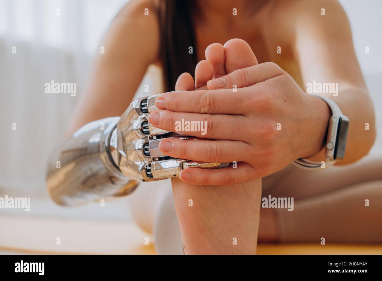 Femme gaie avec bras de prothèse bionique en métal fait des exercices d'étirement sur le sol près du lit dans la chambre ensoleillée à proximité Banque D'Images