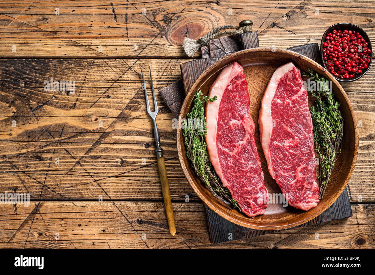 Steaks de viande de boeuf non cuits en haut cru au sommet de sirloin dans une assiette en bois avec des herbes. fond de woden. Vue de dessus. Copier l'espace Banque D'Images