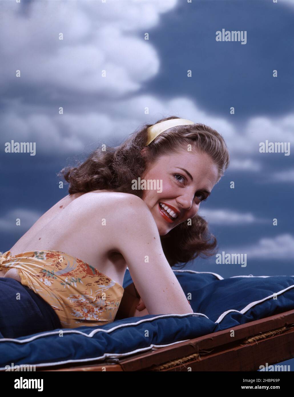 Jeune femme aux cheveux foncés avec un bandeau blanc, allongé sur son  ventre et ses coudes sur une chaise de plage Photo Stock - Alamy
