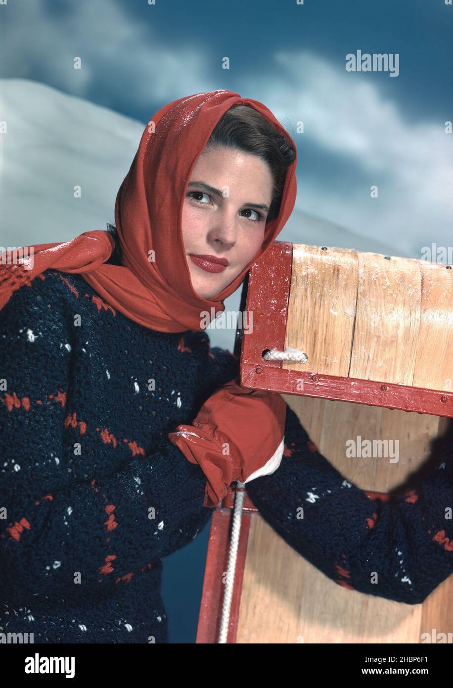 Jeune femme aux cheveux foncés en robe d'hiver et cagoule rouge appuyé contre un toboggan Banque D'Images