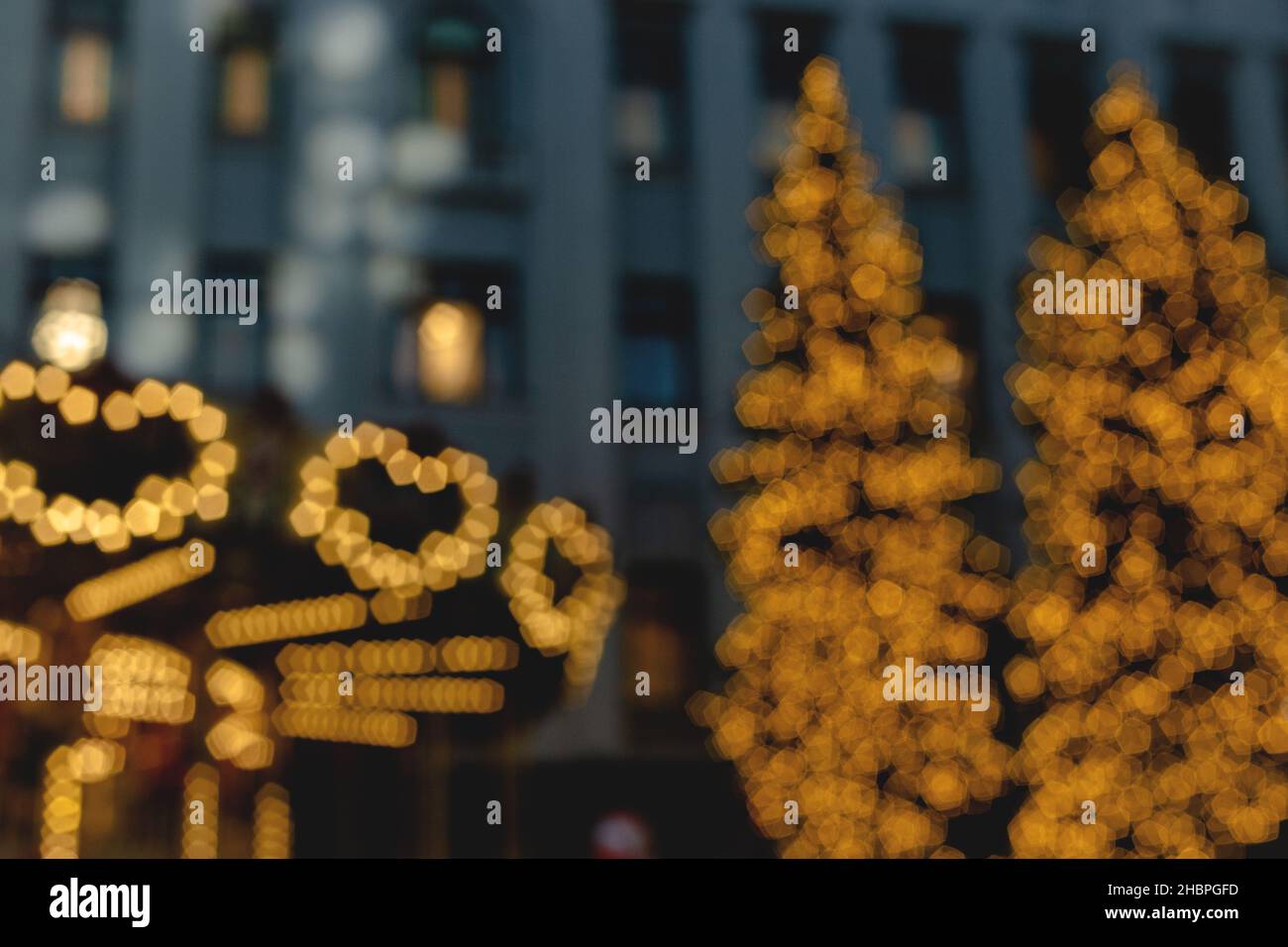 Arbres de Noël et carrousel dans guirlande lumineuse de noël sur fond de bâtiment de plusieurs étages.Image floue.Fond d'écran Banque D'Images