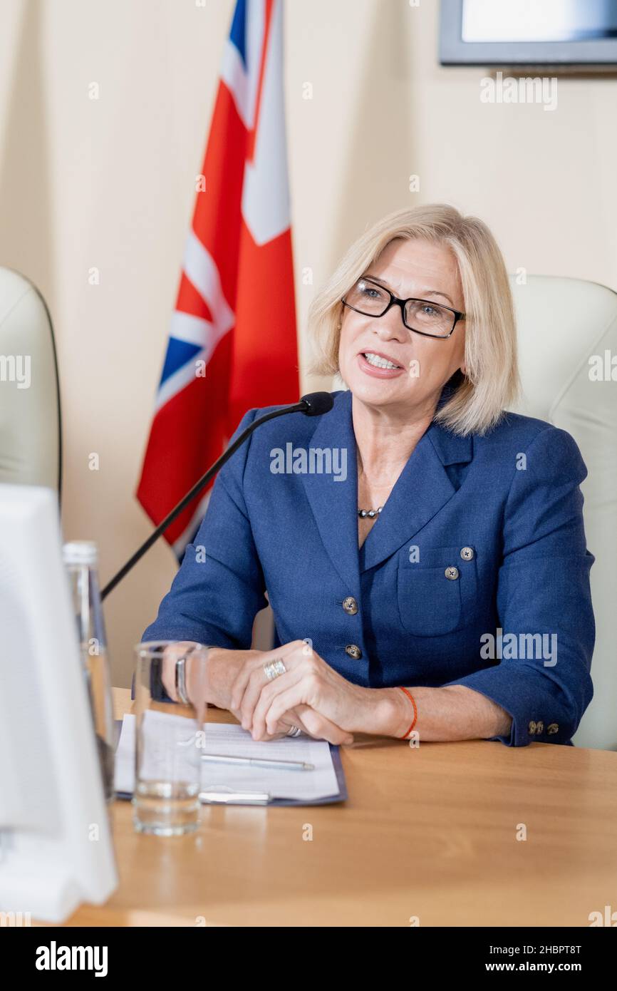 Une femme blonde mûre confiante et confiante qui fait un rapport lors d'une conférence politique tout en étant assise devant le public Banque D'Images