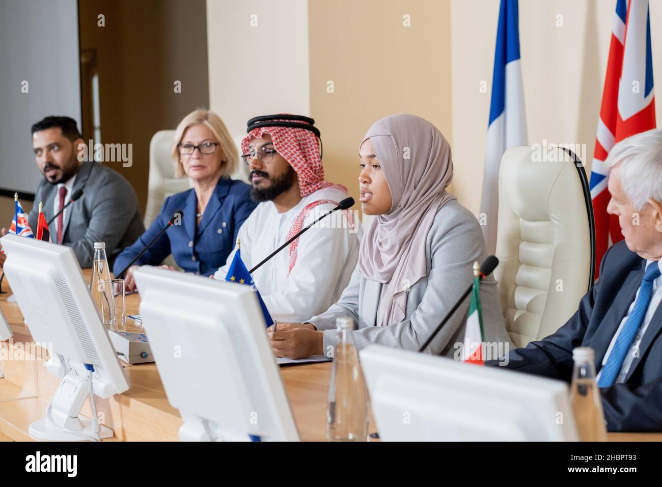Jeune femme musulmane déléguée dans le hijab faisant rapport à des collègues étrangers lors d'un sommet ou d'un forum politique Banque D'Images
