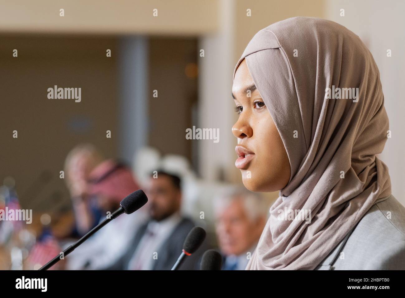 Jeune jolie femme intervenant dans hijab parlant à l'auditoire lors d'une conférence, d'un forum politique ou d'un sommet Banque D'Images